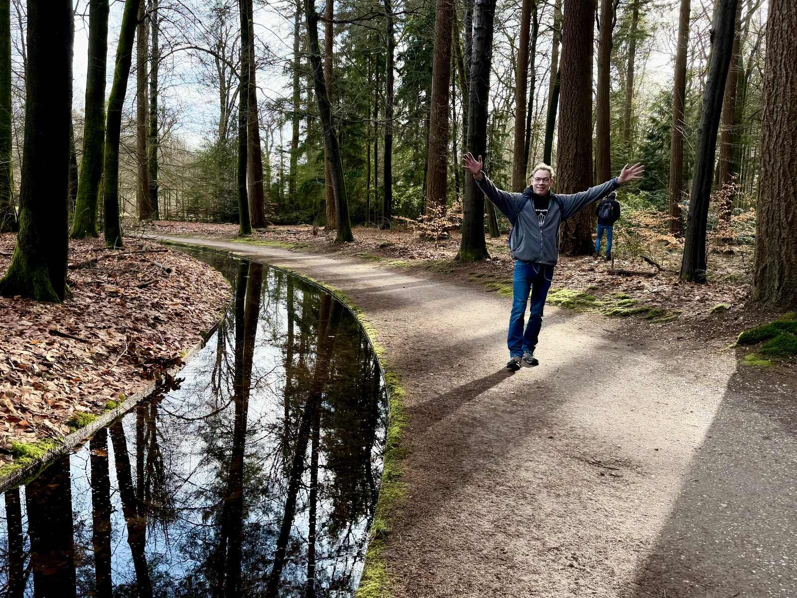 Bok met gespreide armen op een bospad langs een beek